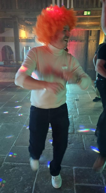 Personne avec perruque orange dansant dans une fête.